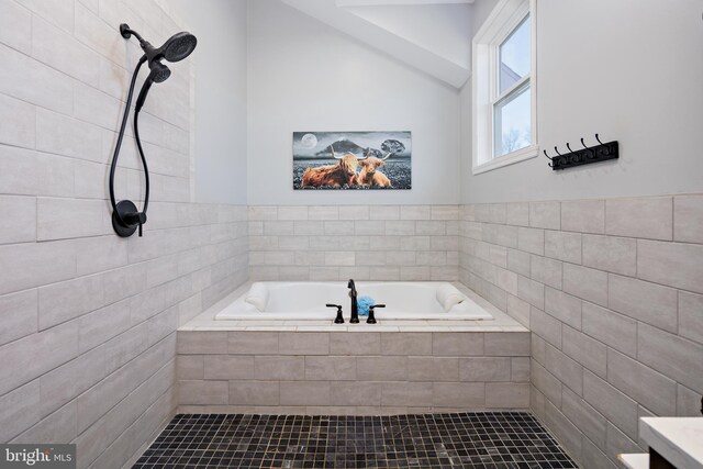 bathroom with a relaxing tiled tub, vaulted ceiling, and tile walls