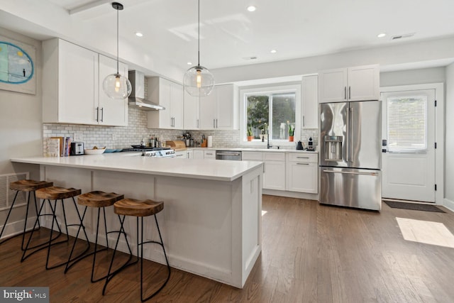 kitchen with appliances with stainless steel finishes, wall chimney range hood, decorative light fixtures, white cabinets, and dark hardwood / wood-style floors