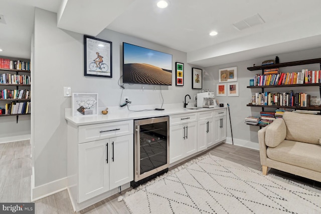 bar with wine cooler, white cabinetry, sink, and light wood-type flooring