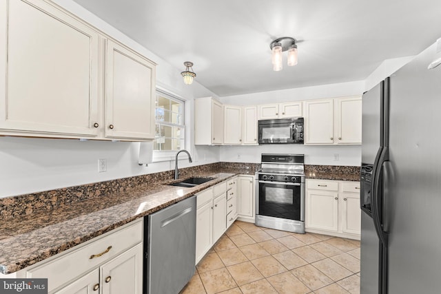 kitchen with appliances with stainless steel finishes, sink, light tile patterned floors, dark stone countertops, and white cabinets