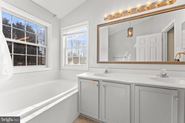 bathroom with vanity, a relaxing tiled tub, and vaulted ceiling