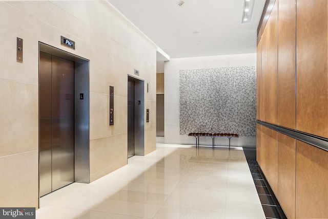 hallway with light tile patterned floors, elevator, and tile walls