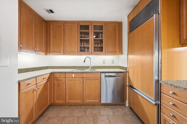 kitchen with light stone countertops, paneled fridge, sink, dishwasher, and light tile patterned flooring