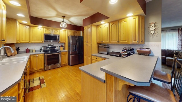 kitchen with sink, stainless steel appliances, light hardwood / wood-style flooring, kitchen peninsula, and a breakfast bar