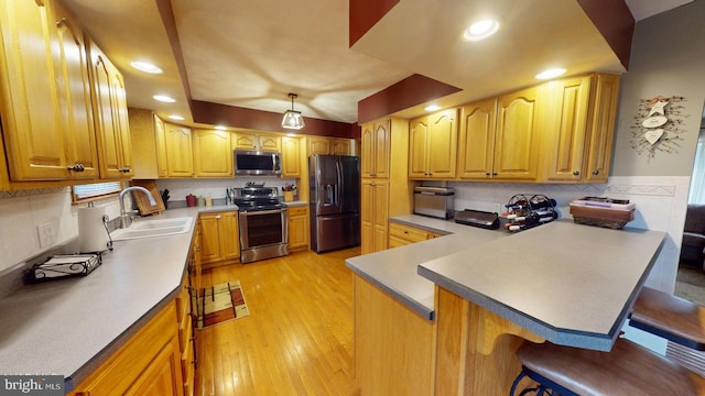 kitchen featuring sink, stainless steel appliances, light hardwood / wood-style flooring, kitchen peninsula, and a kitchen bar