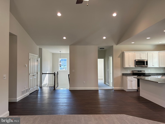 kitchen with dark wood-type flooring, vaulted ceiling, light stone countertops, white cabinetry, and stainless steel appliances