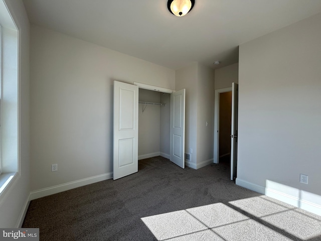 unfurnished bedroom with dark colored carpet and a closet