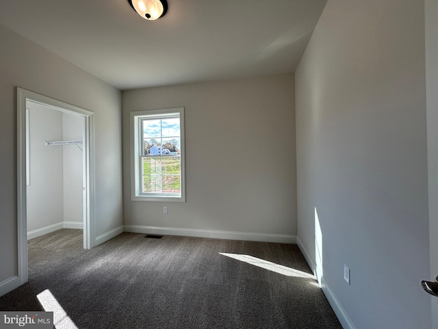 unfurnished bedroom featuring a walk in closet, dark carpet, and a closet