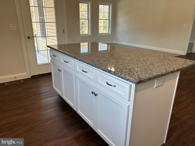 kitchen with white cabinets, a kitchen island, dark hardwood / wood-style flooring, and dark stone countertops