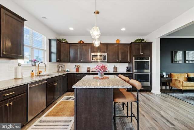 kitchen featuring appliances with stainless steel finishes, sink, a center island, light hardwood / wood-style floors, and hanging light fixtures