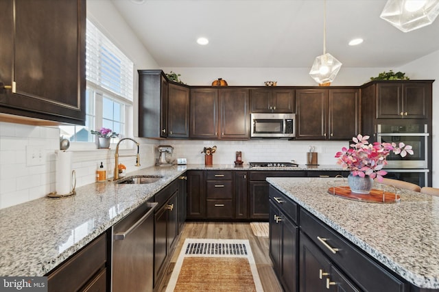 kitchen with sink, hanging light fixtures, stainless steel appliances, decorative backsplash, and light wood-type flooring