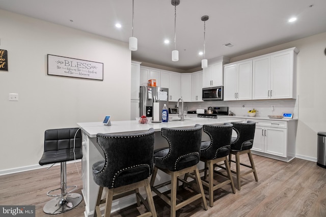 kitchen with stainless steel appliances, decorative light fixtures, light hardwood / wood-style flooring, white cabinets, and an island with sink