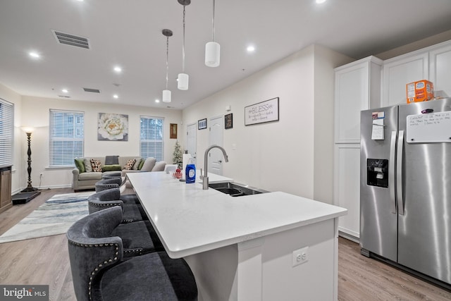 kitchen featuring stainless steel fridge with ice dispenser, sink, white cabinets, and a kitchen island with sink