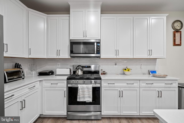 kitchen featuring white cabinets, decorative backsplash, stainless steel appliances, and light hardwood / wood-style flooring