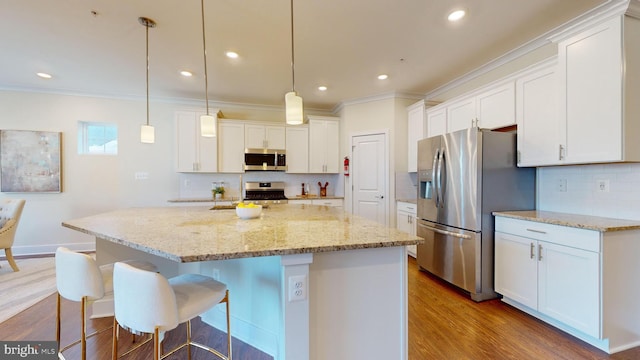 kitchen with appliances with stainless steel finishes, wood-type flooring, a center island, white cabinetry, and hanging light fixtures