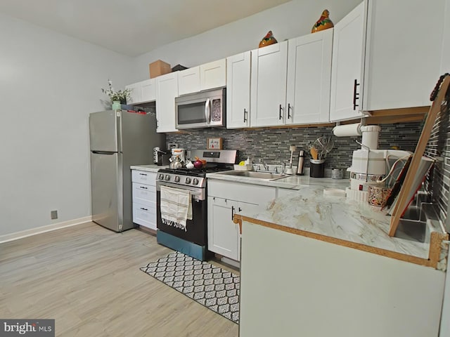 kitchen with decorative backsplash, appliances with stainless steel finishes, sink, light hardwood / wood-style flooring, and white cabinetry