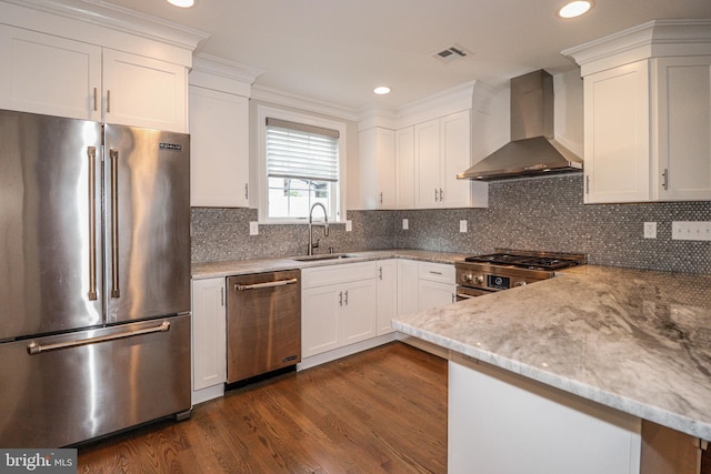 kitchen with light stone countertops, wall chimney exhaust hood, stainless steel appliances, sink, and white cabinets