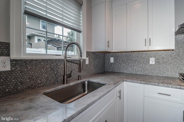 kitchen featuring white cabinets, decorative backsplash, light stone counters, and sink