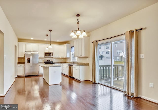 kitchen with hanging light fixtures, stainless steel appliances, a healthy amount of sunlight, a kitchen island, and white cabinetry