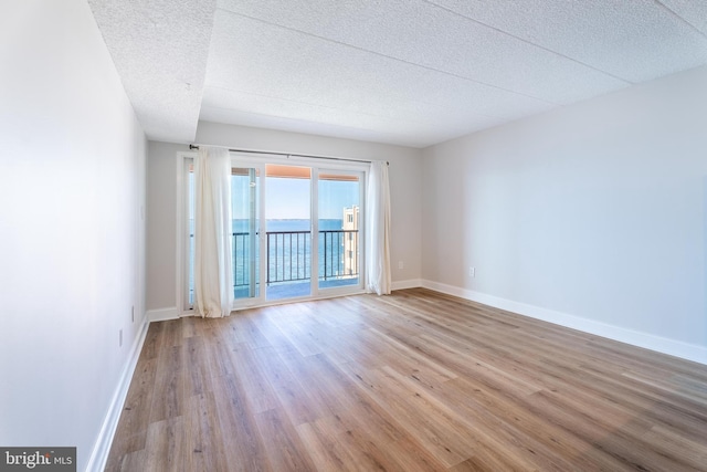 empty room with a textured ceiling, baseboards, and wood finished floors