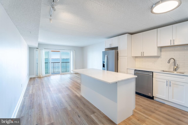 kitchen with light wood-style flooring, a sink, appliances with stainless steel finishes, white cabinets, and decorative backsplash