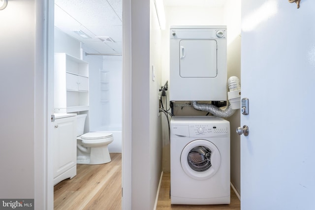 laundry area with light hardwood / wood-style flooring and stacked washer and clothes dryer