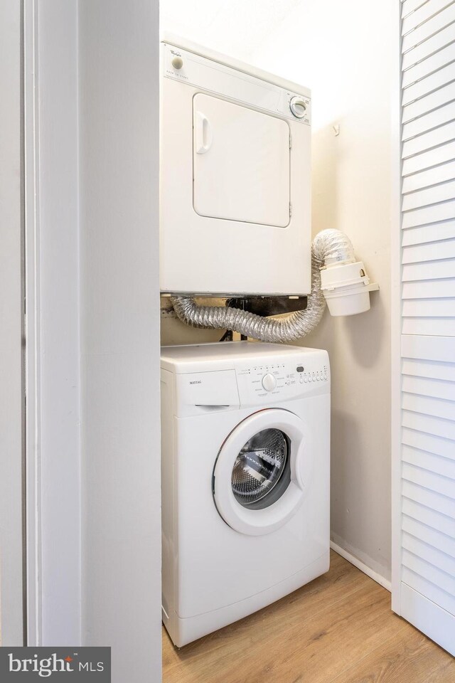 laundry room featuring laundry area, stacked washer / dryer, and light wood-style flooring