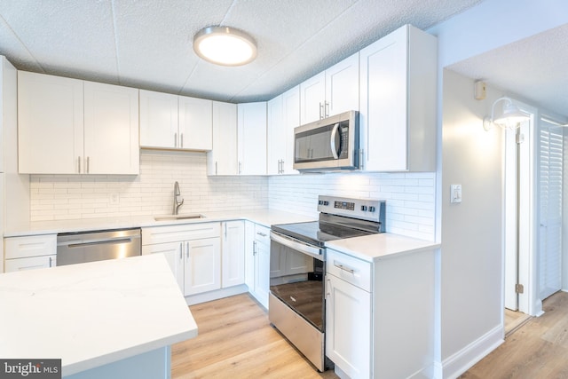 kitchen with light countertops, light wood-style flooring, stainless steel appliances, white cabinetry, and a sink