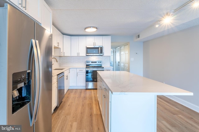 kitchen featuring visible vents, a kitchen island, a sink, stainless steel appliances, and tasteful backsplash