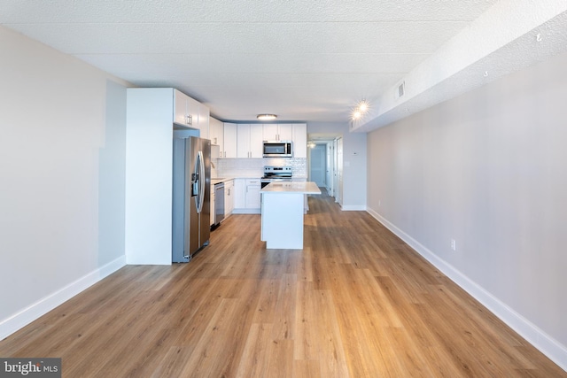 kitchen with light wood-style flooring, light countertops, appliances with stainless steel finishes, white cabinetry, and tasteful backsplash