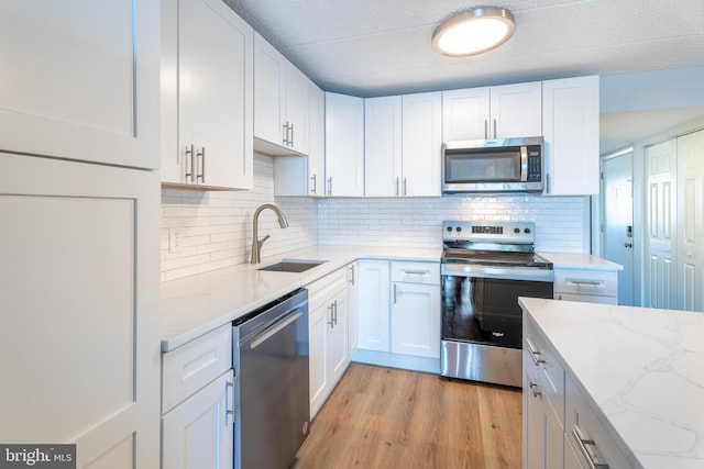 kitchen featuring a sink, stainless steel appliances, light wood-style floors, white cabinets, and light stone countertops