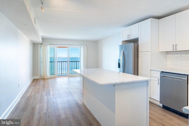 kitchen featuring stainless steel appliances, a kitchen island, decorative backsplash, white cabinets, and light wood-type flooring