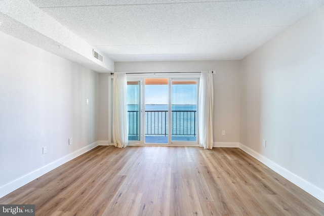 spare room featuring a textured ceiling, baseboards, visible vents, and light wood-type flooring