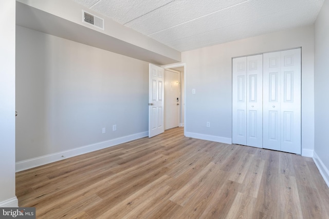 unfurnished bedroom with light wood-style flooring, baseboards, visible vents, and a closet