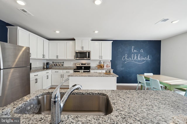 kitchen with light stone countertops, appliances with stainless steel finishes, white cabinetry, and sink