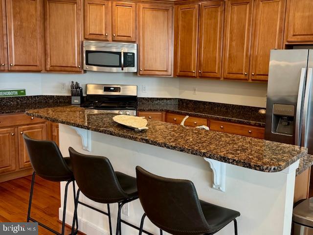 kitchen with a center island, a kitchen breakfast bar, dark stone countertops, appliances with stainless steel finishes, and wood-type flooring