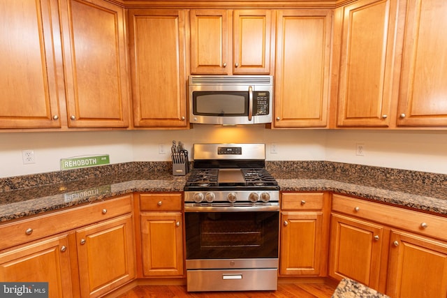 kitchen featuring stainless steel appliances, dark stone counters, and light hardwood / wood-style flooring