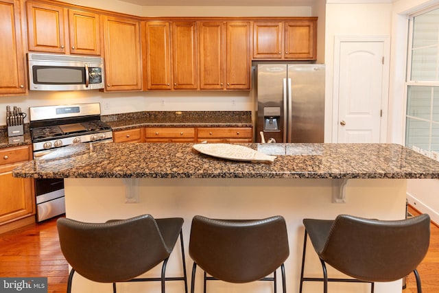 kitchen featuring appliances with stainless steel finishes, dark stone counters, a breakfast bar, wood-type flooring, and a center island