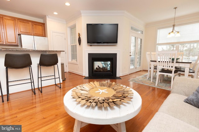 living room featuring an inviting chandelier, ornamental molding, and light hardwood / wood-style flooring