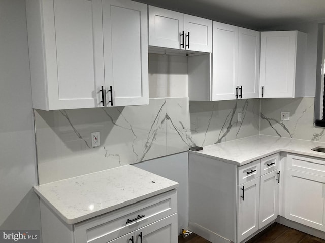 kitchen with white cabinets, tasteful backsplash, light stone countertops, and dark wood-type flooring