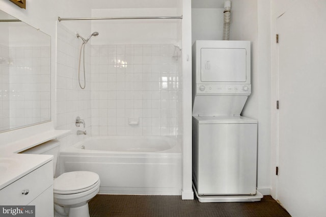 full bathroom featuring vanity, tiled shower / bath combo, stacked washer / dryer, tile patterned flooring, and toilet