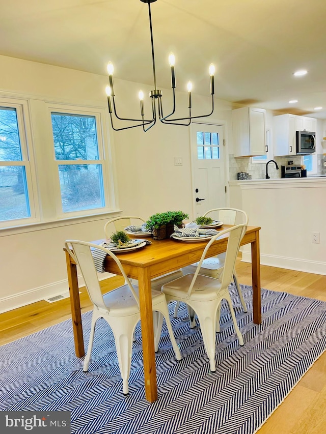 dining area with sink, light hardwood / wood-style flooring, a wealth of natural light, and an inviting chandelier