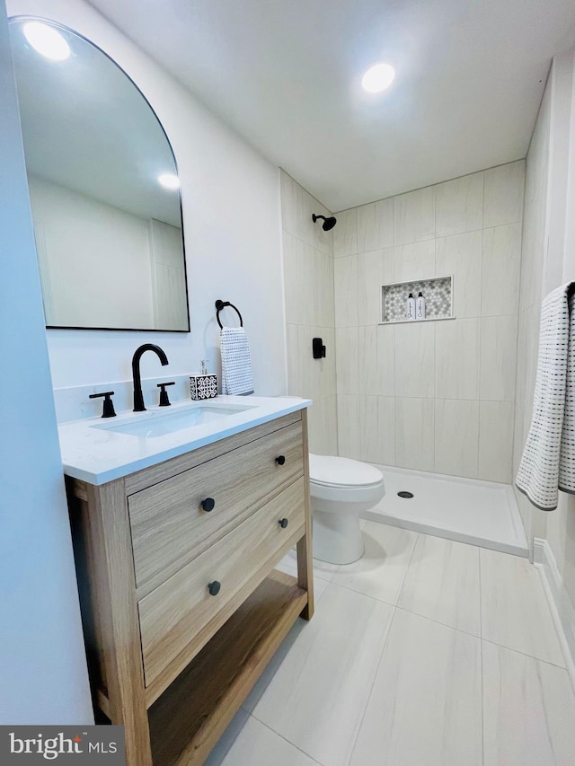 bathroom featuring tiled shower, vanity, toilet, and tile patterned flooring