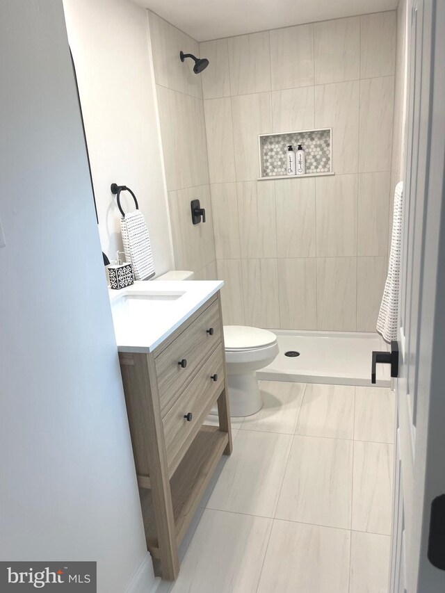 bathroom with tiled shower, tile patterned floors, vanity, and toilet