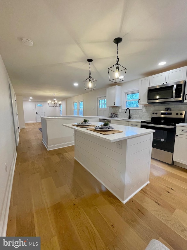 kitchen featuring decorative backsplash, appliances with stainless steel finishes, decorative light fixtures, white cabinetry, and a kitchen island