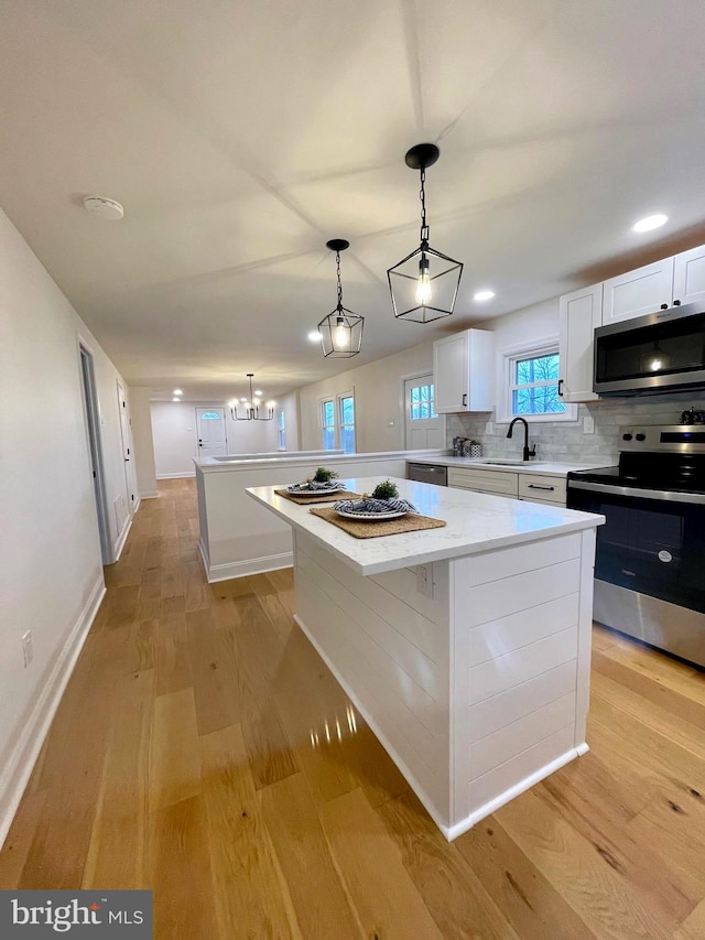 kitchen featuring a center island, white cabinetry, stainless steel appliances, and hanging light fixtures