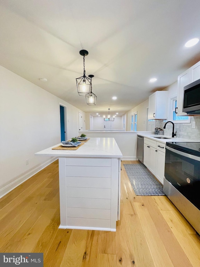 kitchen with a center island, white cabinets, sink, hanging light fixtures, and stainless steel appliances