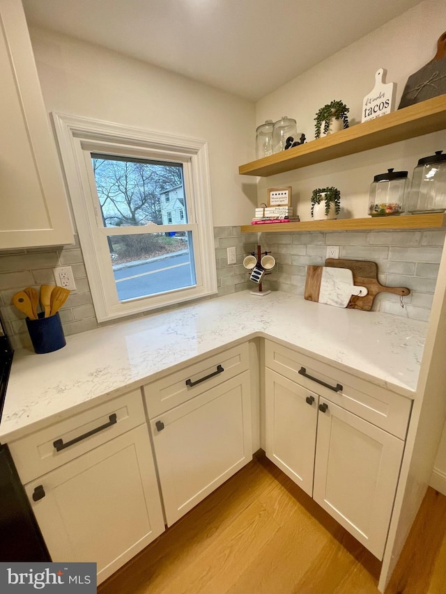 interior space featuring tasteful backsplash, light stone counters, light hardwood / wood-style flooring, and white cabinetry