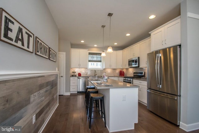 kitchen with appliances with stainless steel finishes, pendant lighting, a center island, dark hardwood / wood-style floors, and white cabinetry