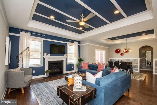 living room with ornamental molding, a raised ceiling, ceiling fan, and dark wood-type flooring